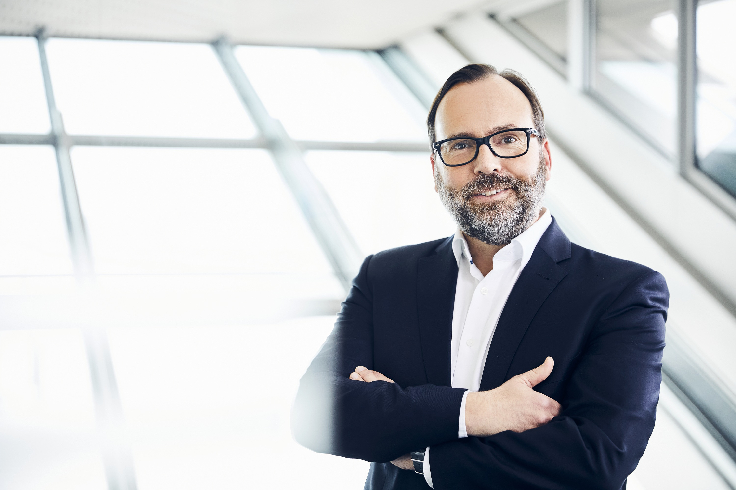 Pressefoto von Jörg Kubitza im Business-Outfit vor modernem Hintergrund