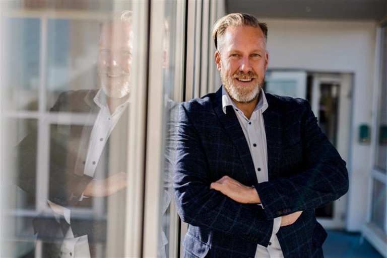 Ingo Mahl steht mit verschränkten Armen an einer Glasfassade und blickt nach draußen