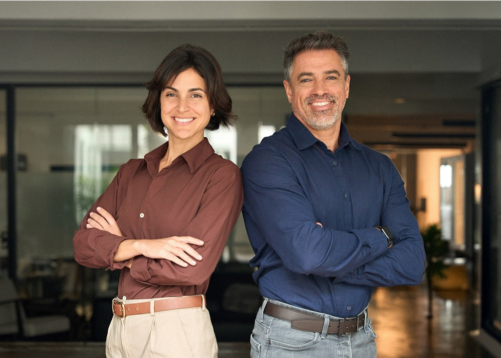 Zwei Geschäftsleute mit verschränkten Armen stehen selbstbewusst nebeneinander im Büro, adobestock-1890038659-web