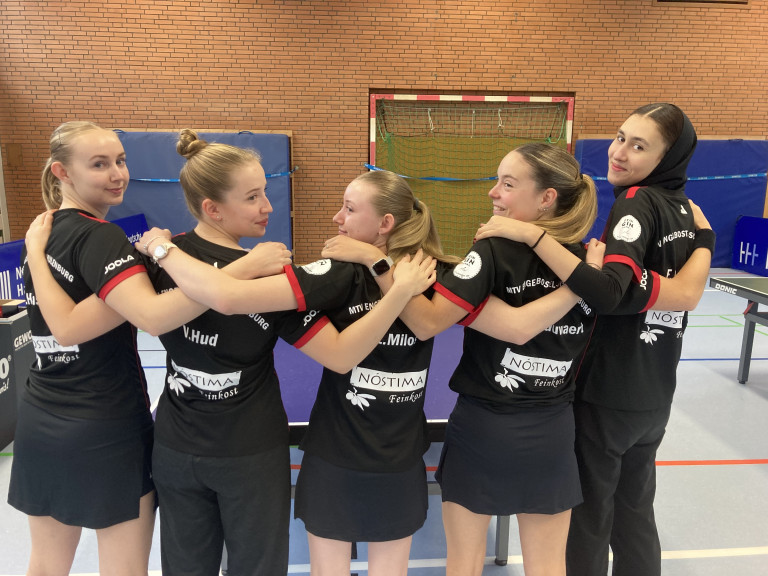 Tischtennis Damenmannschaft MTV Engelbostel-Schulenburg steht in der Sporthalle Arm in Arm vor einem Handballtor