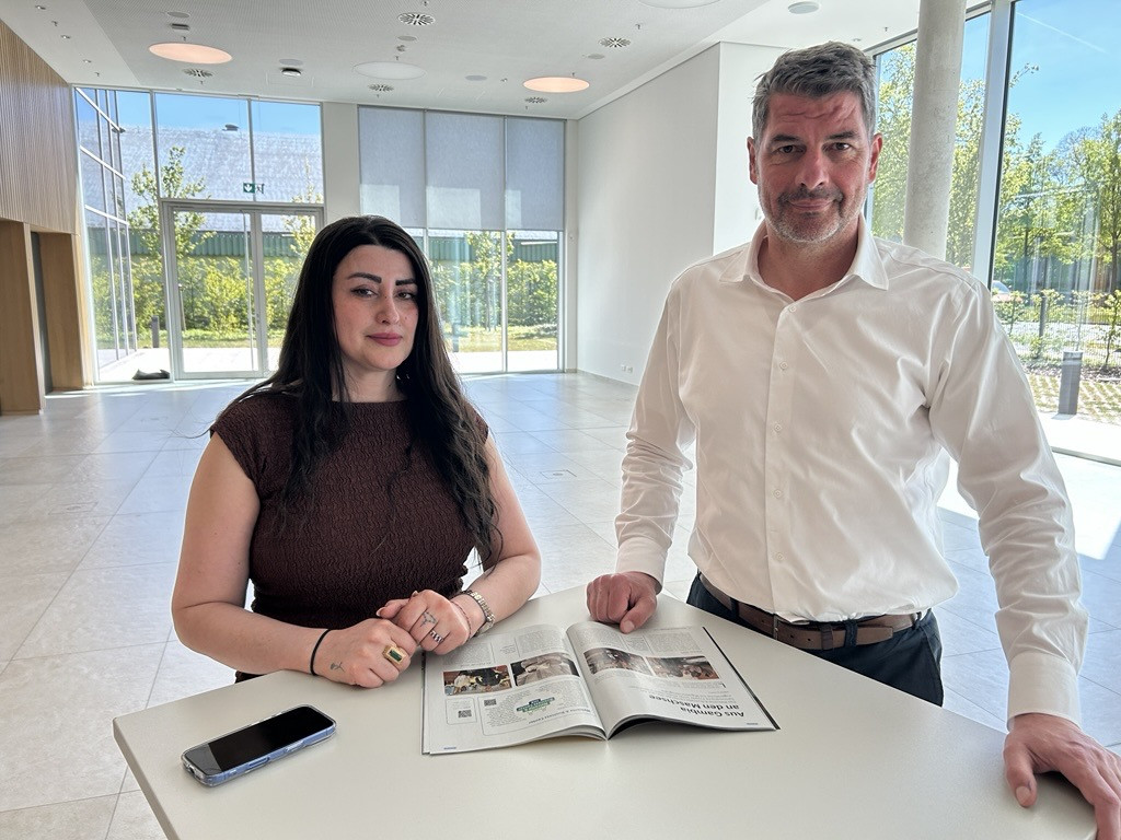 Zwei Personen lesen einen WBC-Artikel in einer modernen, hellen Umgebung, Zeitschrift offen auf dem Tisch, Smartphone daneben.