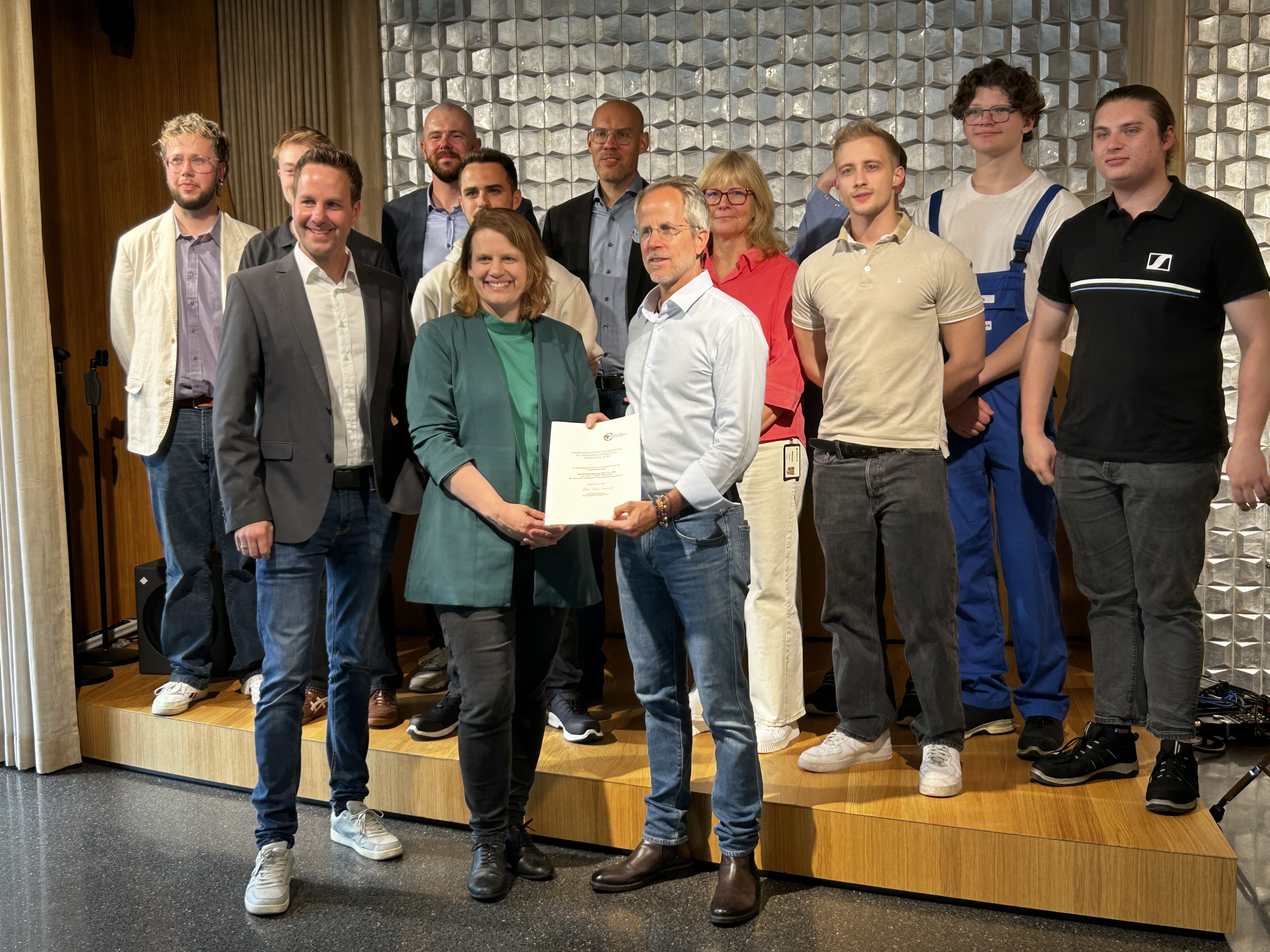 Gruppenfoto einer feierlichen Zertifikatsübergabe mit mehreren Personen auf einer Bühne