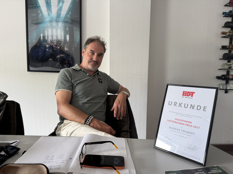 Markus Thunert mit Discotheken Unternehmer-Preis 2017 Urkunde vom BDT im Büro Mann mit Urkunde des Discotheken Unternehmer-Preises 2017 vom BDT im Büro