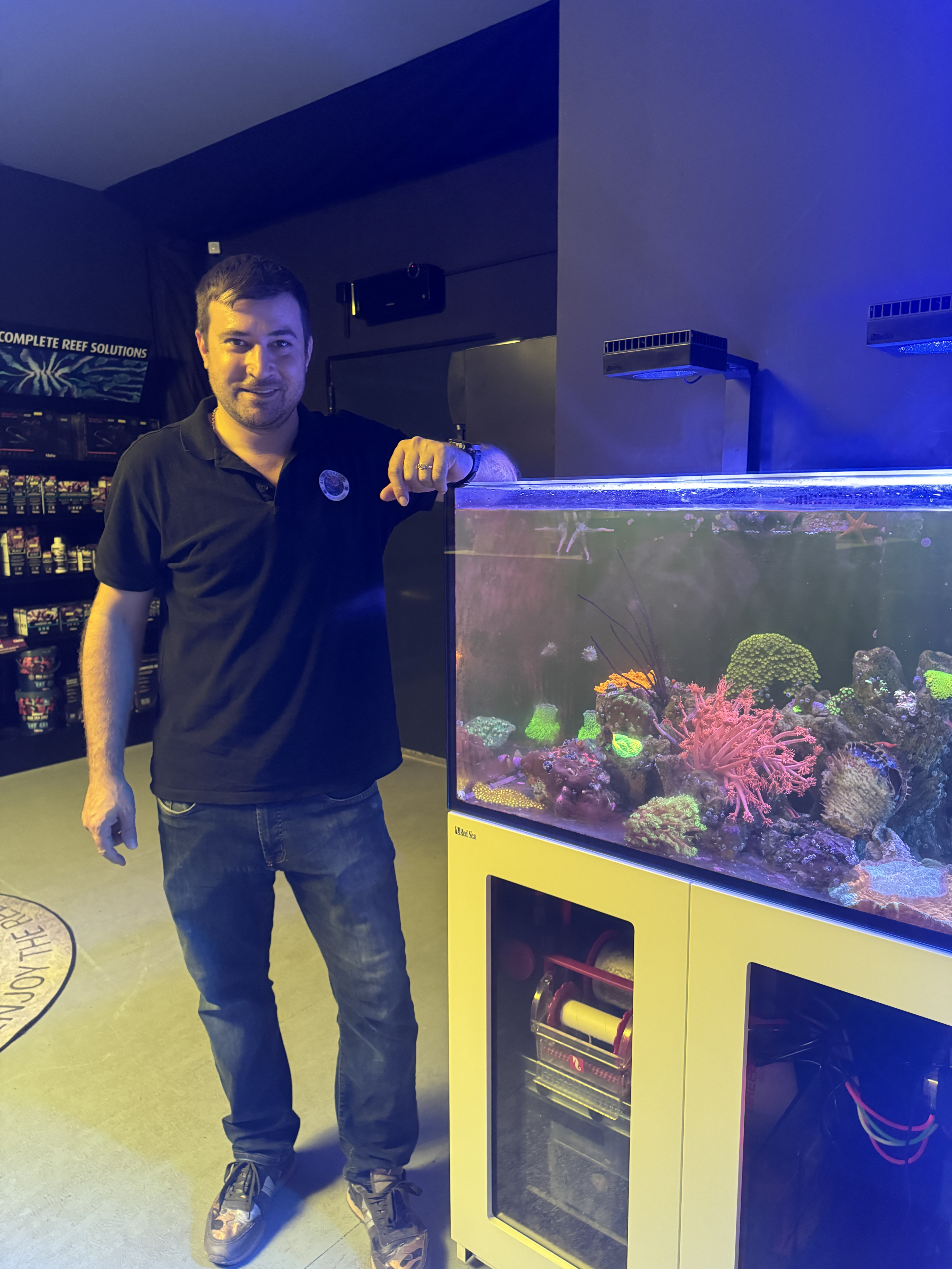 Mann steht neben einem Meerwasseraquarium in einem Aquaristik-Fachgeschäft