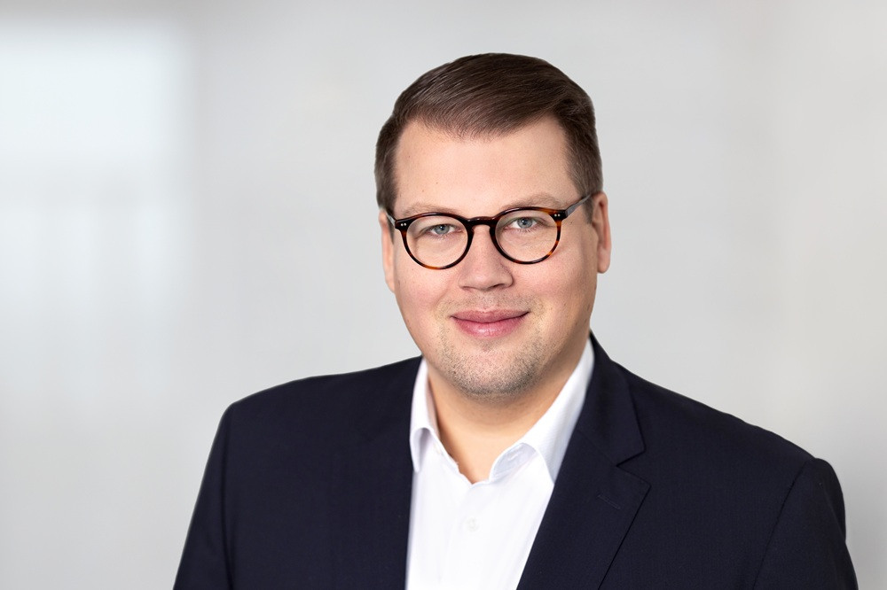 Porträt von Alexander Krause mit Brille und Anzug vor hellem Hintergrund