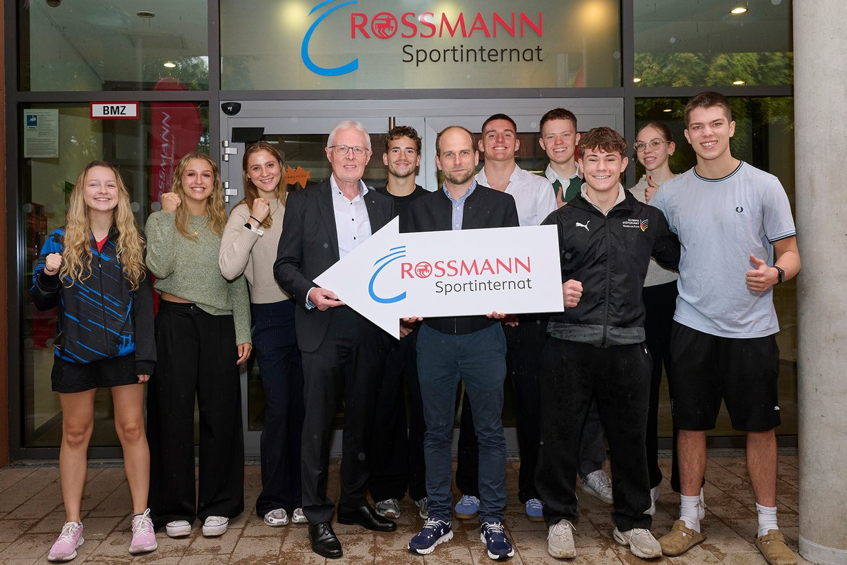 Gruppenfoto vor dem Rossmann Sportinternat mit Jugendlichen und Verantwortlichen, die ein Schild mit dem Logo halten