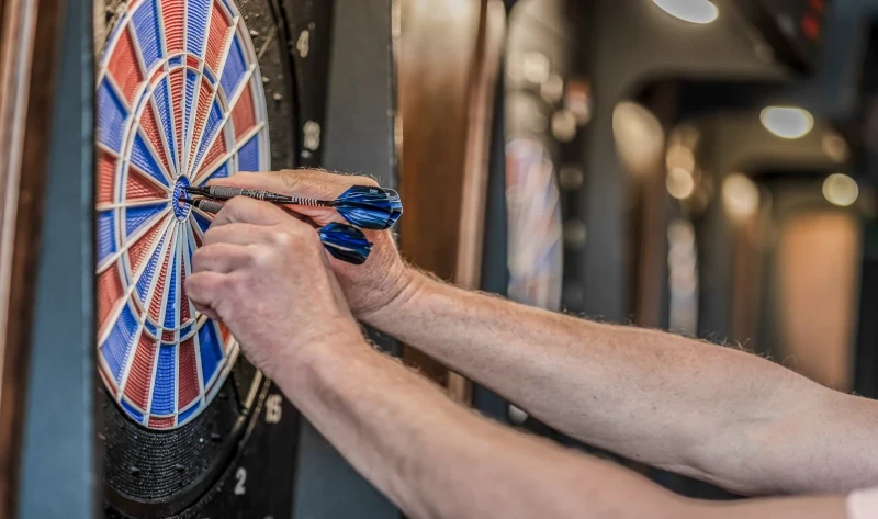 Nahaufnahme von Händen, die Dartpfeile aus einer Dartscheibe ziehen