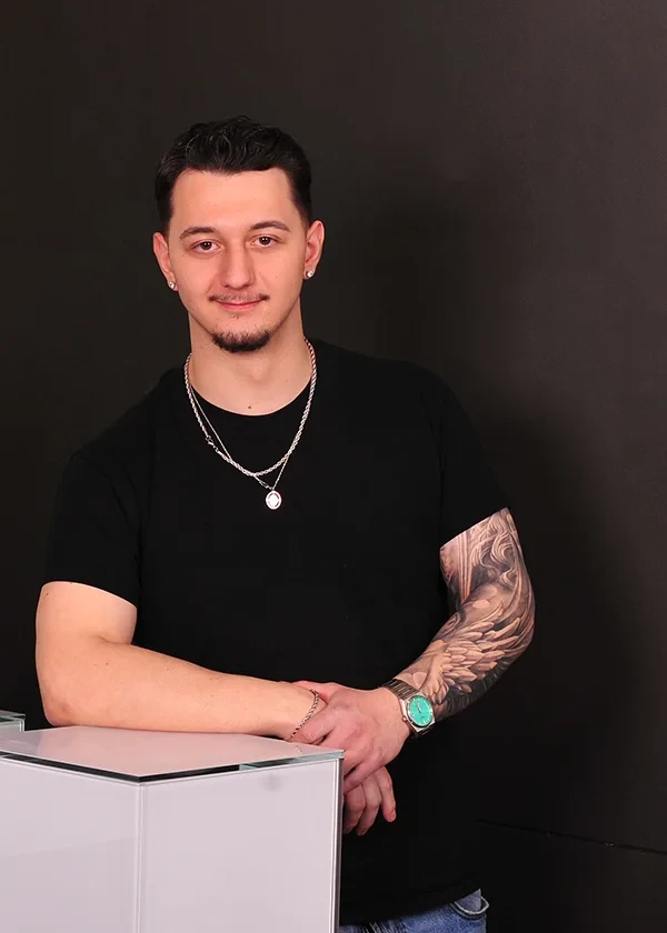 Porträt von Alex mit schwarzem T-Shirt und sichtbarem Tattoo am Arm