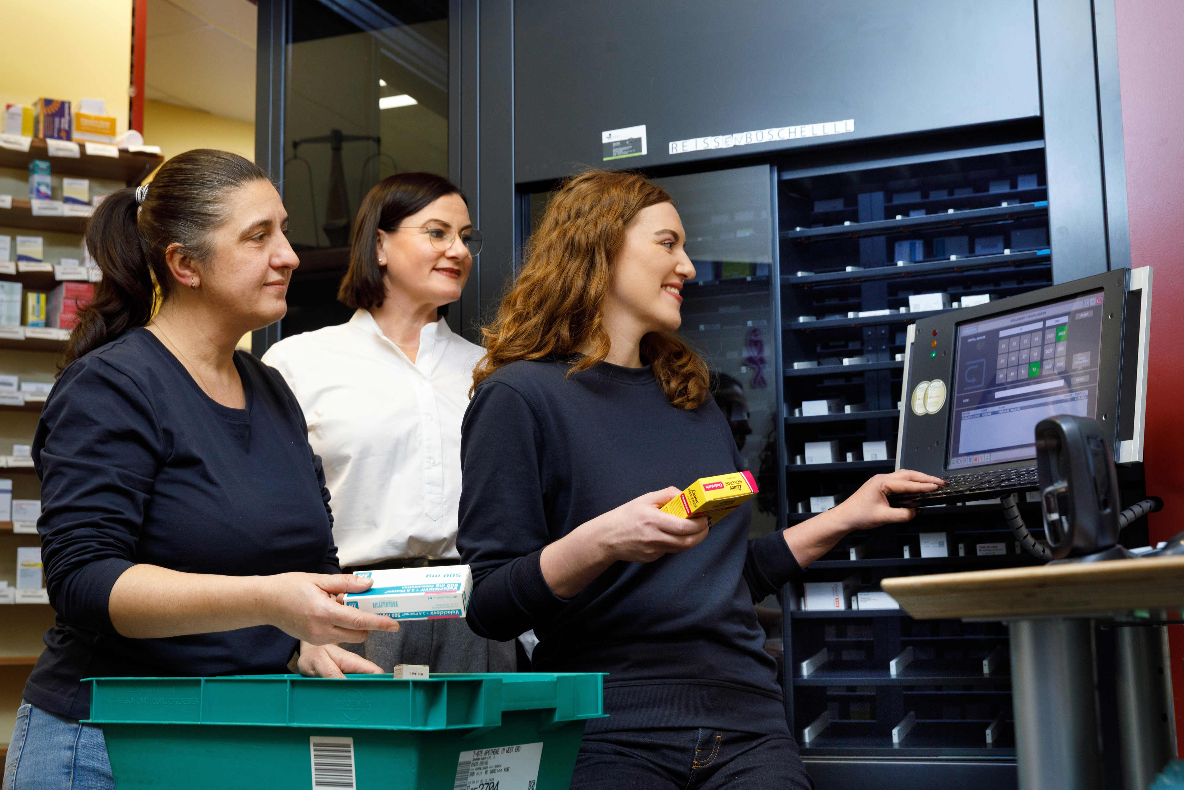 Mitarbeiterinnen in einer Apotheke bedienen ein automatisiertes Lagersystem und sortieren Medikamente