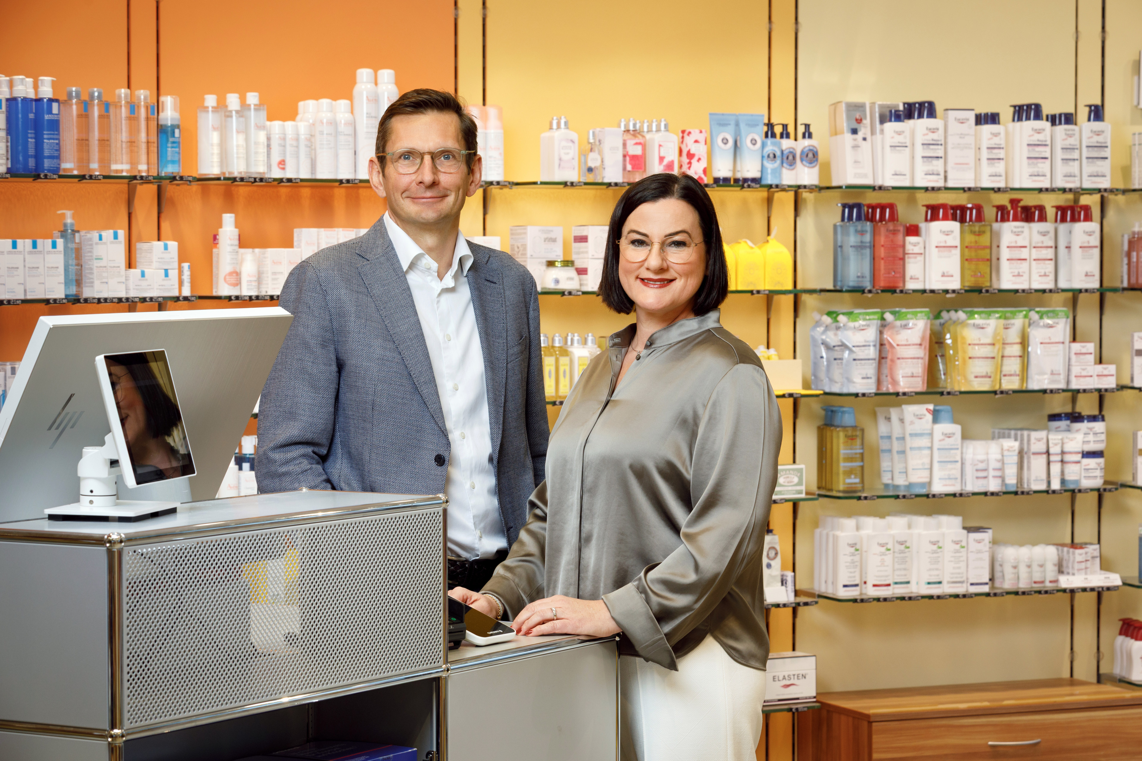 cg-7080-korr: Zwei Personen in einer modernen Apotheke oder Drogerie vor einem Regal mit Kosmetik- und Pflegeprodukten