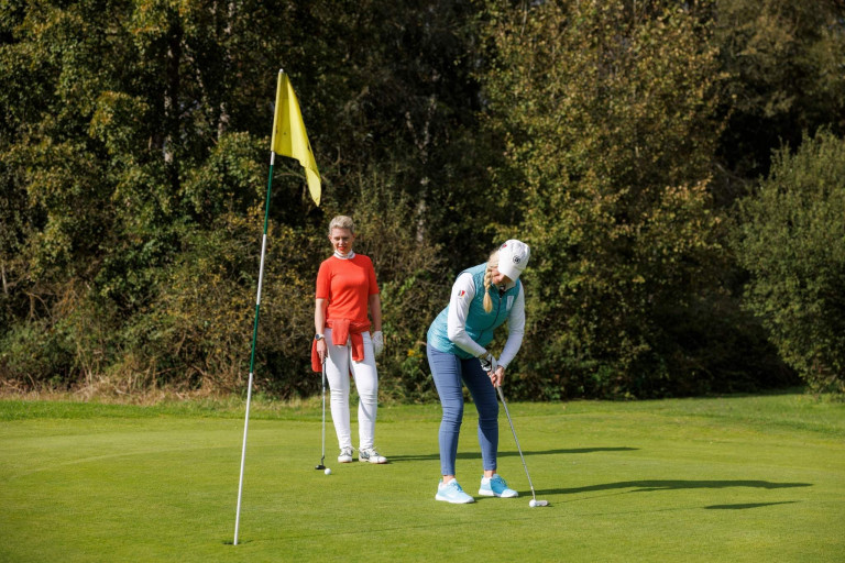 Zwei Golfspielerinnen putten auf dem Grün bei sonnigem Wetter