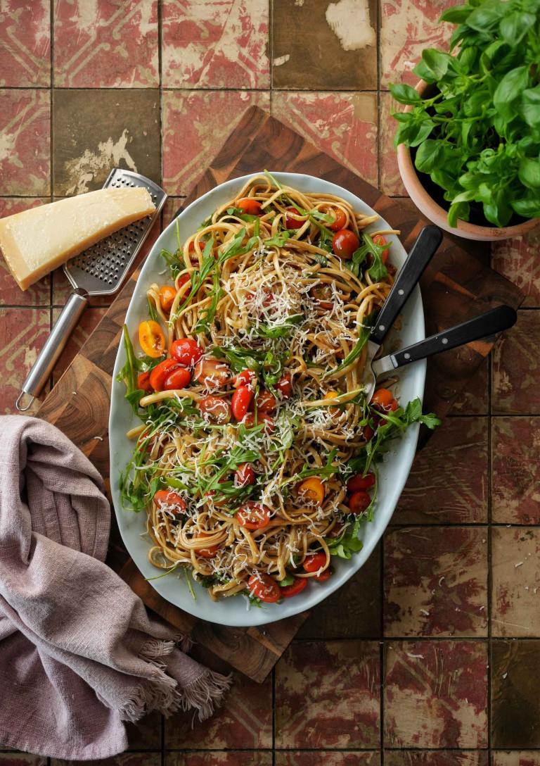 Pasta mit Rucola und Tomaten auf einem Tisch mit Parmesan und Basilikum
