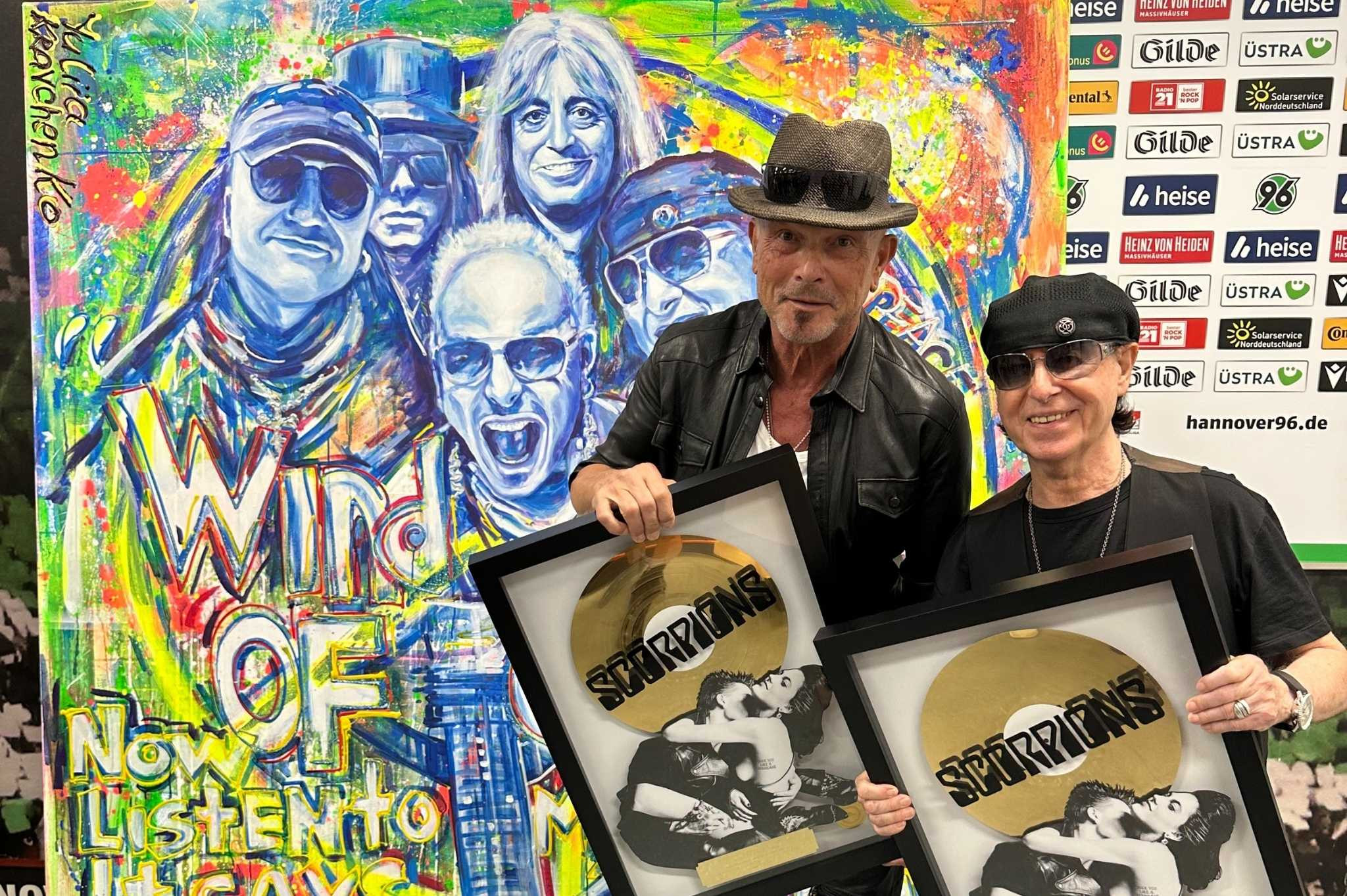 Scorpions erhalten Gold-Auszeichnung – Bandmitglieder mit Schallplatten vor Kunstwerk Mitglieder der Band Scorpions mit goldenen Schallplatten-Auszeichnungen vor buntem Hintergrund