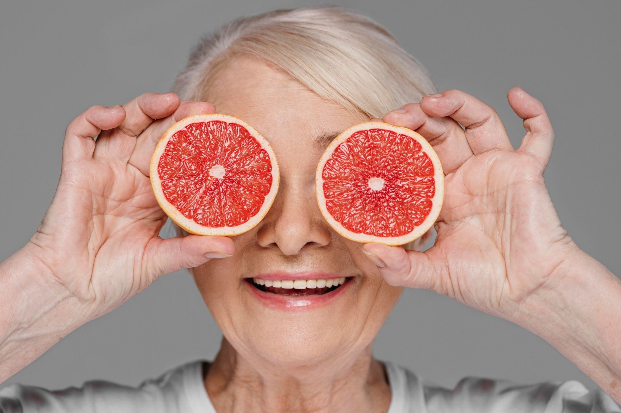 Longevity Aufmacher: Gesunde Ernährung und Langlebigkeit mit Grapefruit Ältere Person hält zwei Hälften einer Grapefruit als Symbol für Langlebigkeit und gesunde Ernährung