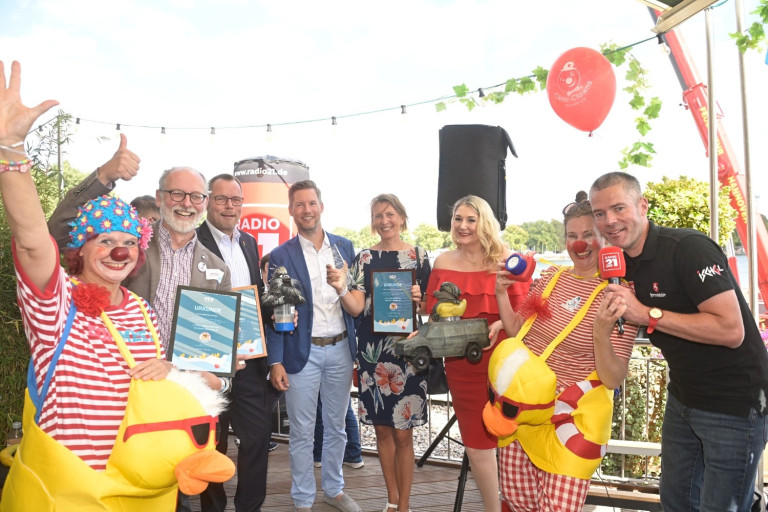 Gruppenfoto bei einer Preisverleihung mit Urkunden, Radio 21 Branding und Clown, aufgenommen am 16.08.2025