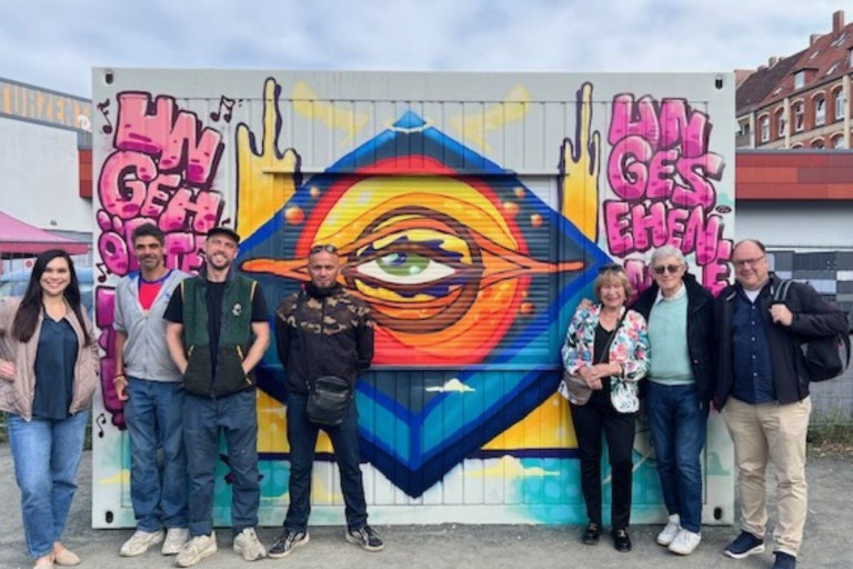 Personengruppe vor Container mit farbenfrohem Graffiti und Auge-Motiv