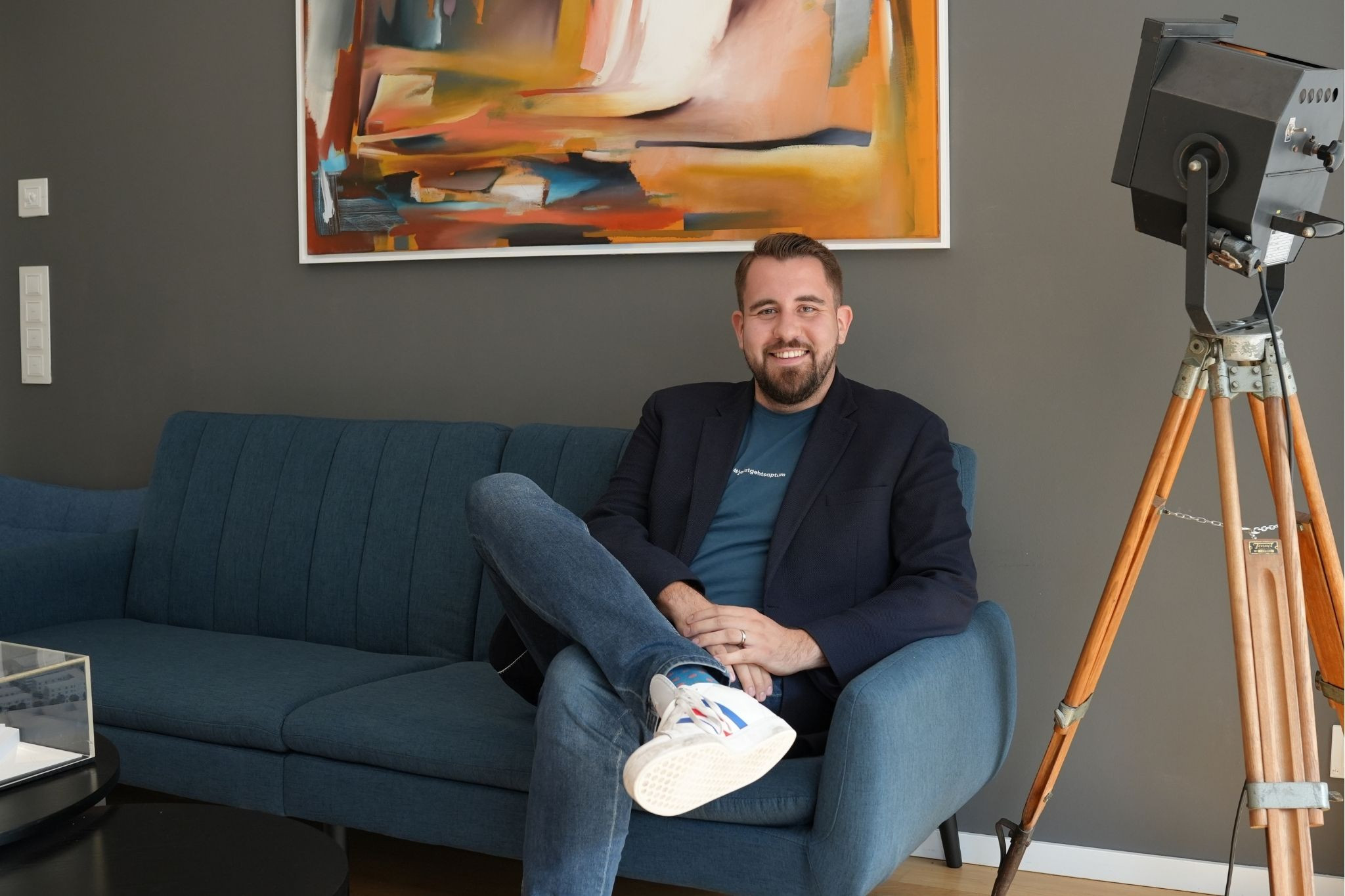 Domik Talhof sitzt entspannt auf einem blauen Sofa vor einem modernen Gemälde