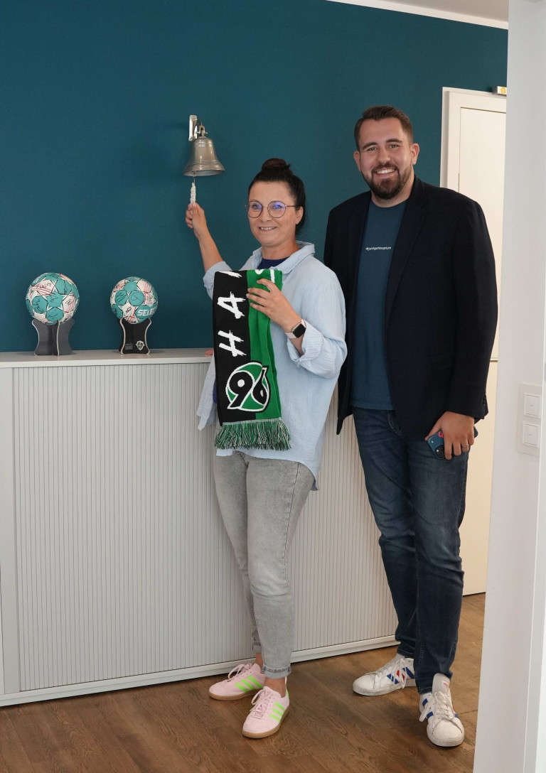 Dominik Talhof mit Hannover 96 Fanschal vor einer Wand mit Fußball-Souvenirs und Glocke