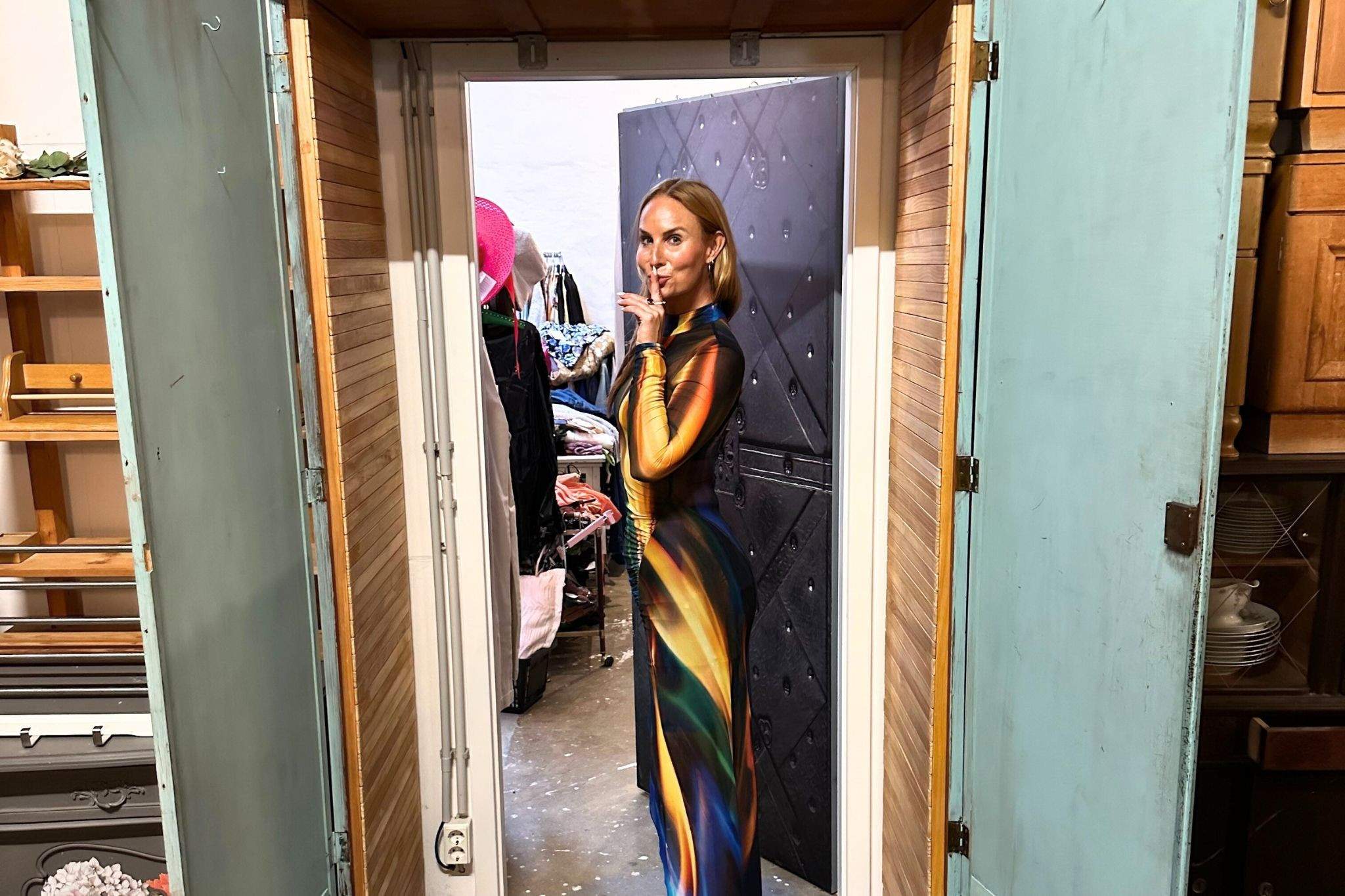 Frau in farbenfrohem Kleid posiert für eine Stilkolumne in einem Secondhand-Laden