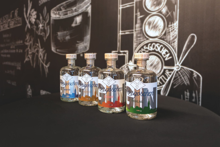 Vier verschiedene Rossgoschen Gin Sorten aus Hannover auf einem Tisch vor einer Tafel mit Logo