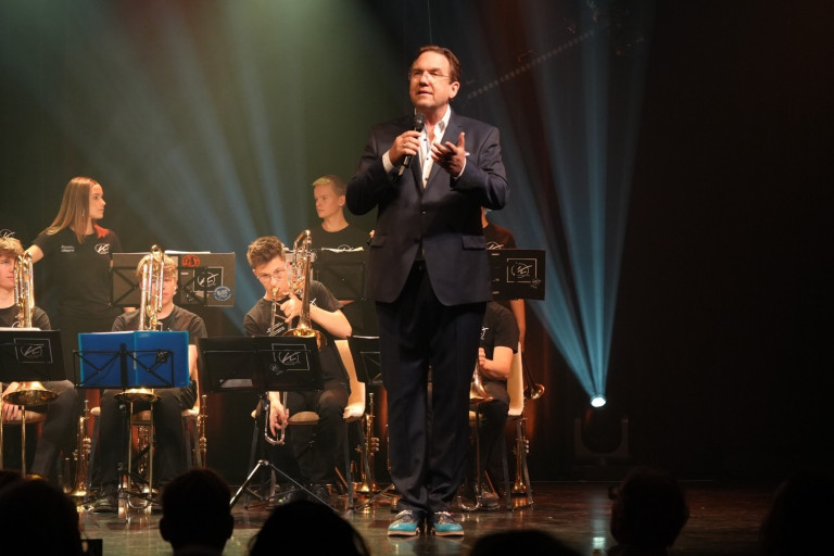 Moderator bei der Benefizgala der Niedergerke Stiftung 2025 auf der Bühne mit Orchester Moderator spricht auf der Bühne bei der Benefizgala der Niedergerke Stiftung 2025 vor einem Orchester