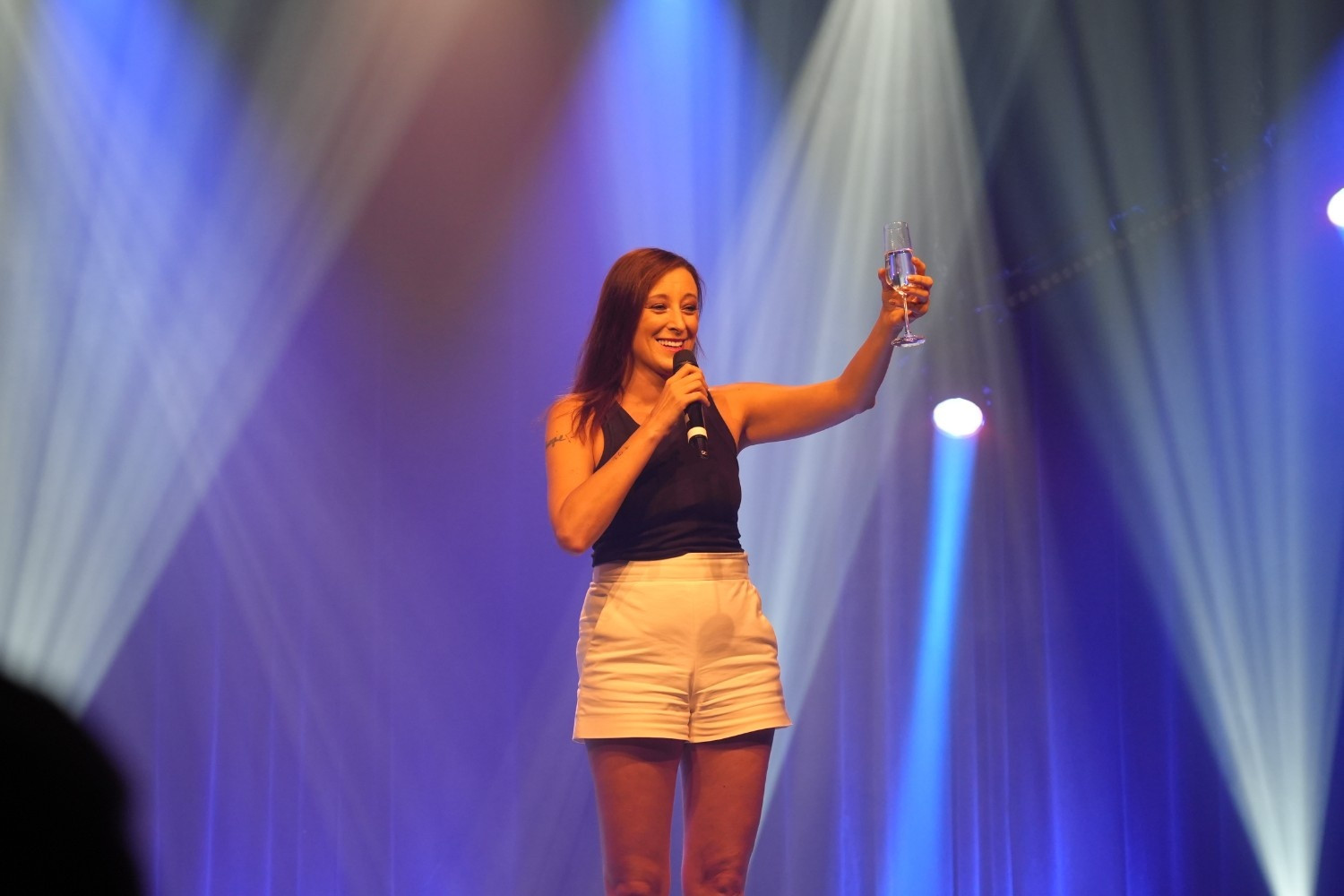 Ansprache auf der Bühne bei der Benefizgala der Niedergerke Stiftung 2025/28 Frau hält eine Ansprache mit Mikrofon und Sektglas auf der Bühne bei der Benefizgala der Niedergerke Stiftung 2025/28
