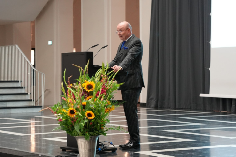 Redner am Podium bei der Verleihung der Karmarsch-Denkmünze 2025, festlich dekoriert mit Blumen