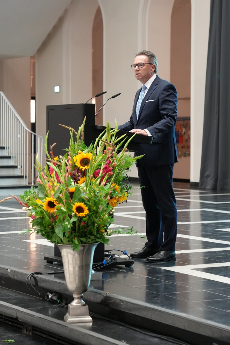 Redner bei der Verleihung der Karmarsch-Denkmünze 2025 am Rednerpult mit Blumenschmuck