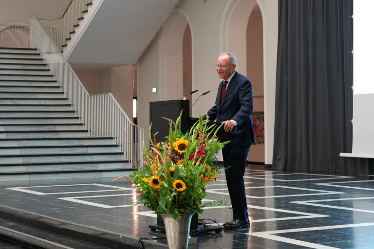 Redner bei der Verleihung der Karmarsch-Denkmünze 2025 am Rednerpult mit Blumenschmuck im Vordergrund