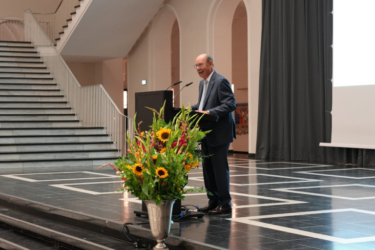 Redner bei der Verleihung der Karmarsch-Denkmünze 2025 auf einer Bühne mit Blumenschmuck