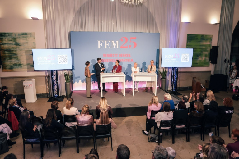 Podiumsdiskussion bei der FEM25 Konferenz mit mehreren Teilnehmern auf der Bhne und Publikum im Saal
