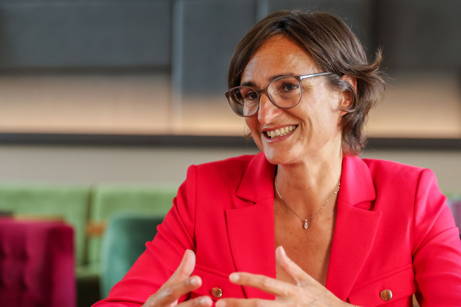 Aurelie im Gespräch, sitzend in modernem Interieur, roter Blazer