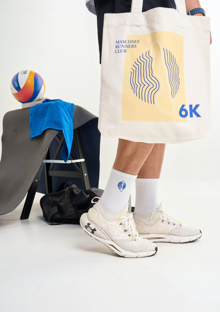Sportliche Szene mit Under Armour Laufschuhen, weißer Sporttasche mit 'Runners Club 6K' Print und Volleyball im Fitnessstudio