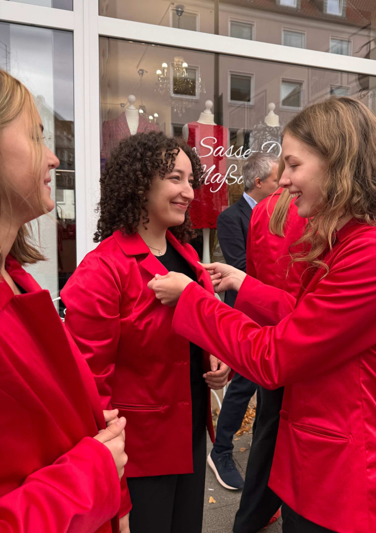 Mädchenchor-Mitglieder im roten Blazer vor einem Geschäft, bereiten sich auf einen Auftritt vor