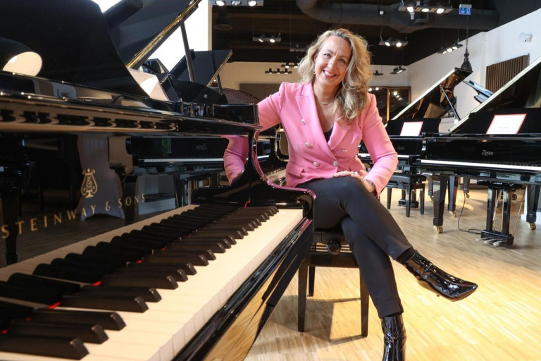 Frau im Klavierhaus Doll sitzt an einem Flügel zwischen mehreren Klavieren