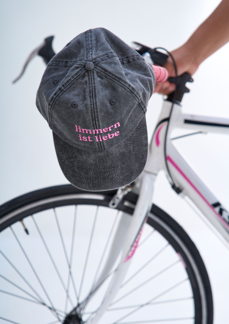 Graue Cap mit pinker Aufschrift 'limmern ist liebe' auf weißem Fahrrad