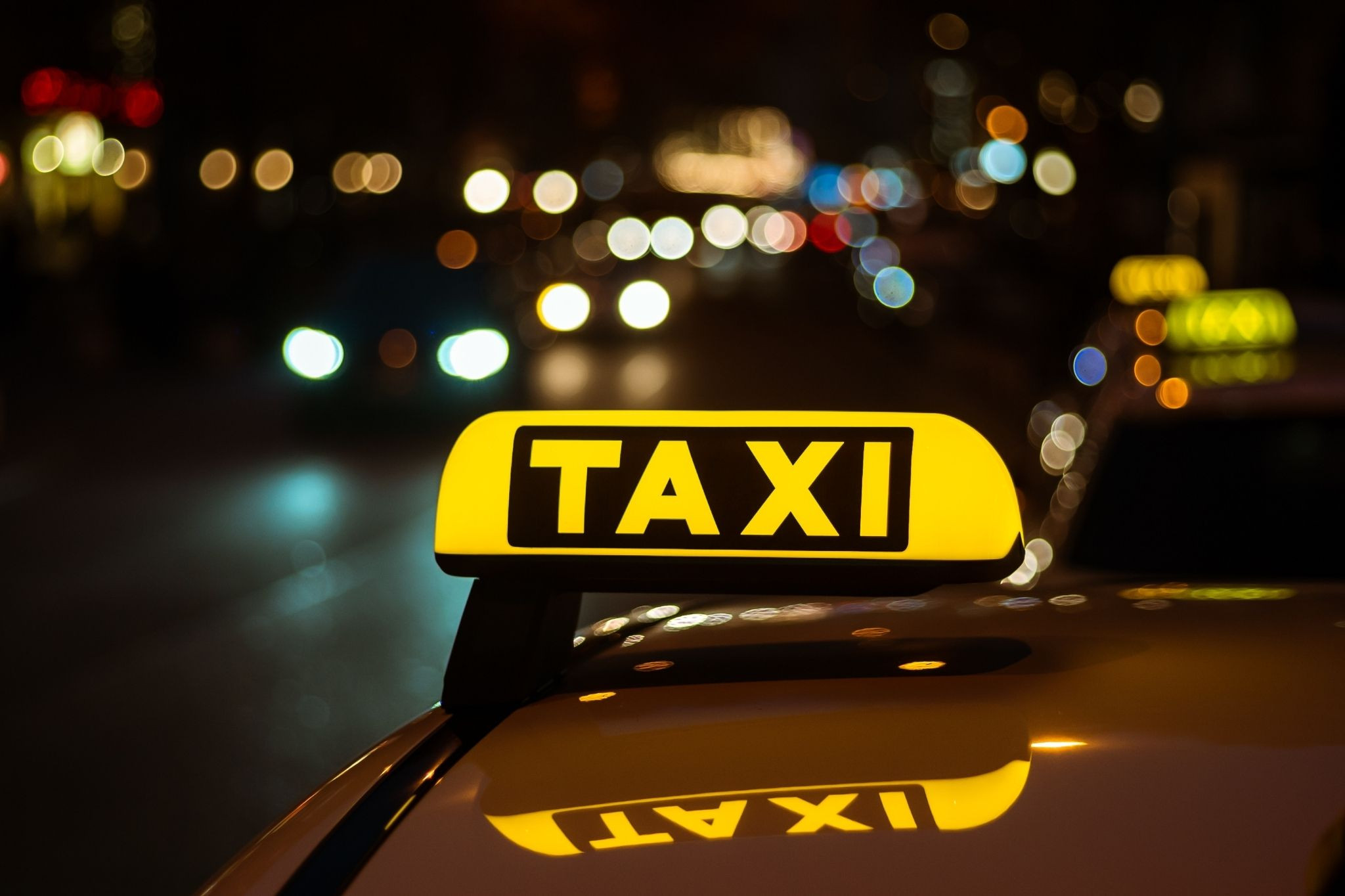 Taxi-Aufmacher: Leuchtendes Taxischild auf einem Auto bei Nacht in der Stadt