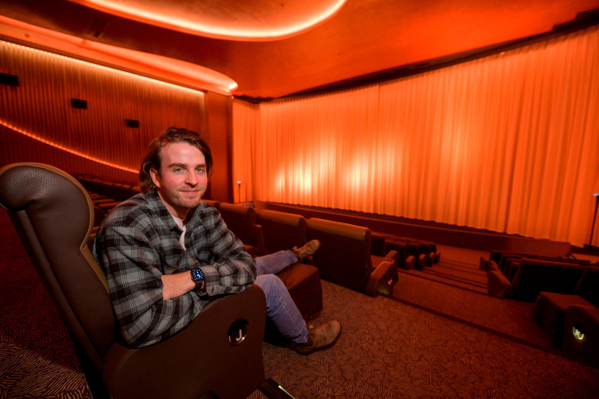 Christoph Basse sitzt entspannt in einem modernen, orange beleuchteten Kinosaal