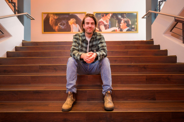 Christoph Basse auf einer Holztreppe in einer Galerie oder öffentlichem Raum Christoph Basse sitzt auf einer Holztreppe vor Bildern in einer Galerie oder einem öffentlichen Gebäude