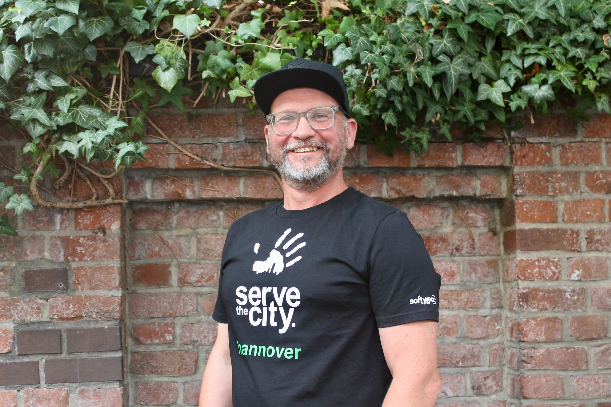 Person mit Serve the City Hannover T-Shirt vor einer Backsteinmauer mit Efeu