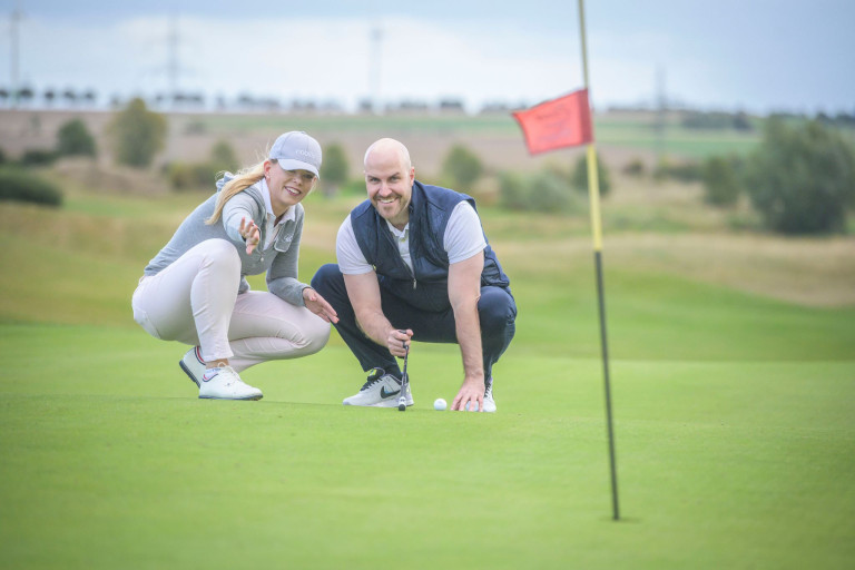 Golfspieler beim Putten auf dem Golfplatz neben einer Fahne Zwei Personen auf dem Golfplatz beim Putten neben einer Fahne
