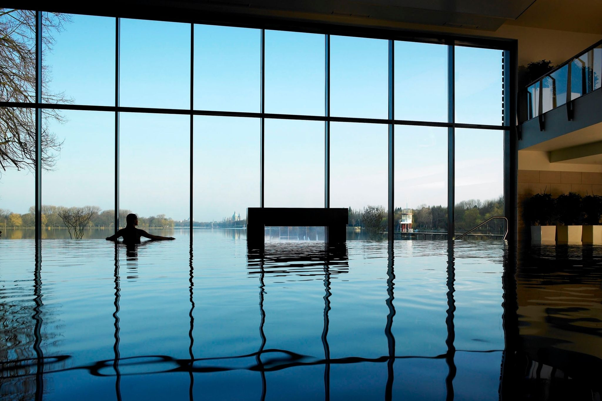 Aufmacher Wellness: Person entspannt im Infinity-Pool mit Panoramablick auf See und Natur