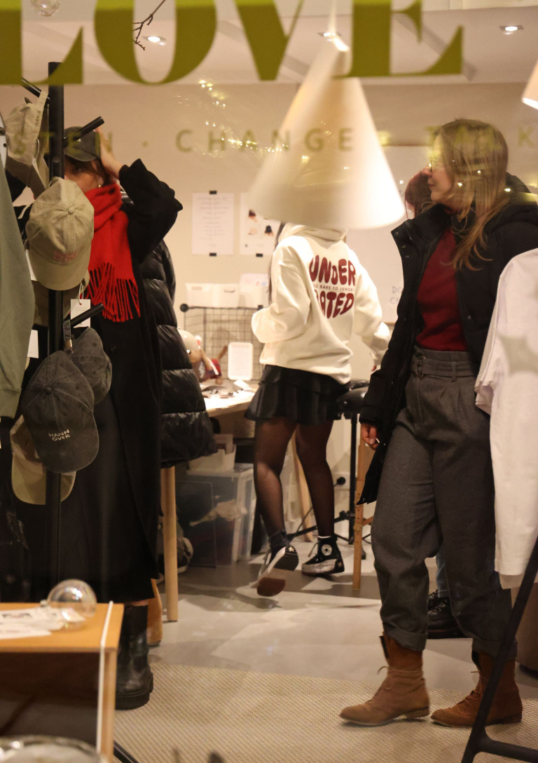 Besucherinnen auf einem modernen Pop-up-Event mit Mode-Accessoires und Streetwear, darunter ein Hoodie mit der Aufschrift 'Underrated'.
