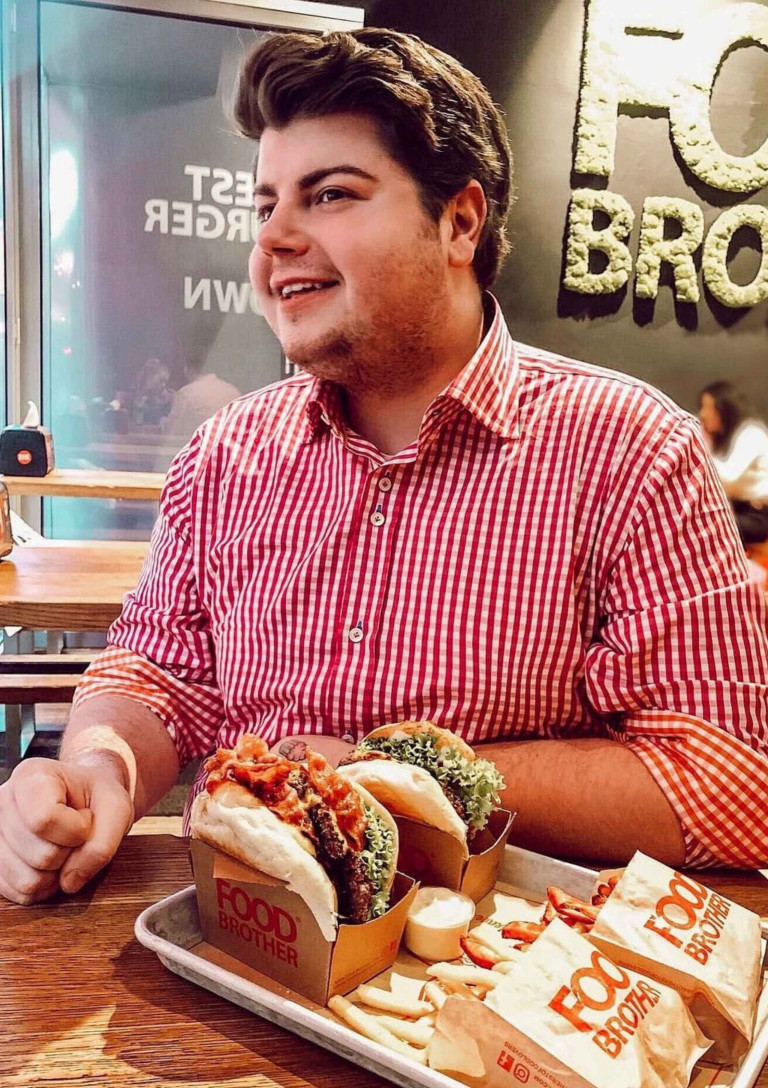 Rene Oliver genießt Burger und Pommes im Restaurant Rene Oliver im Restaurant mit zwei Burgern und Pommes vor sich