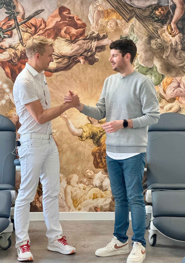 Rene und Oliver beim Handschlag in einer Praxis mit künstlerischer Wandmalerei Rene und Oliver geben sich die Hand in moderner Praxis vor künstlerischer Wandmalerei
