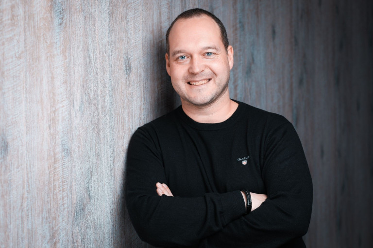 Björn Benke im Esport-Bereich, Person mit verschränkten Armen vor Holzwand