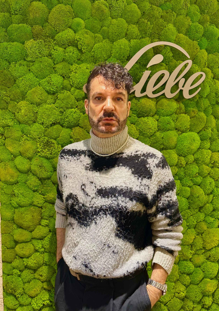 Wintermode: Mann mit modernem Strickpullover vor Mooswand mit Schriftzug 'Liebe'