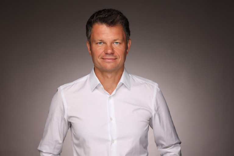 Portrait von Alexander Perbone in weißem Hemd vor neutralem Hintergrund