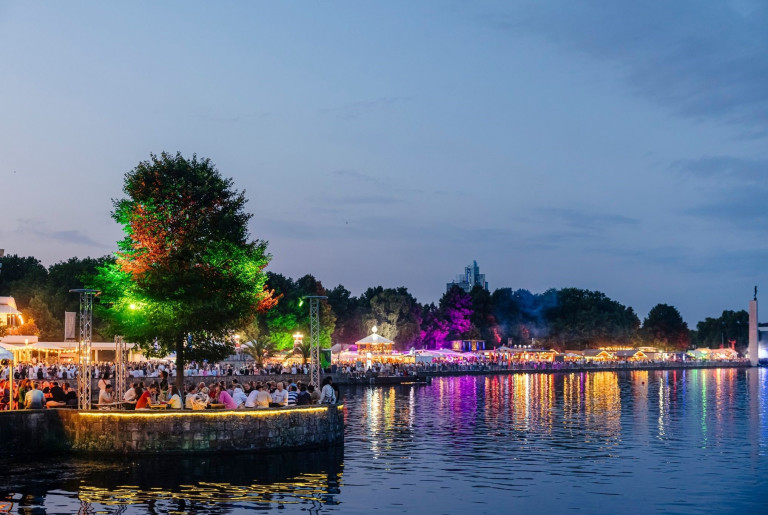 Abendliches Event am See mit bunten Lichtern und vielen Menschen im Jahr 2026