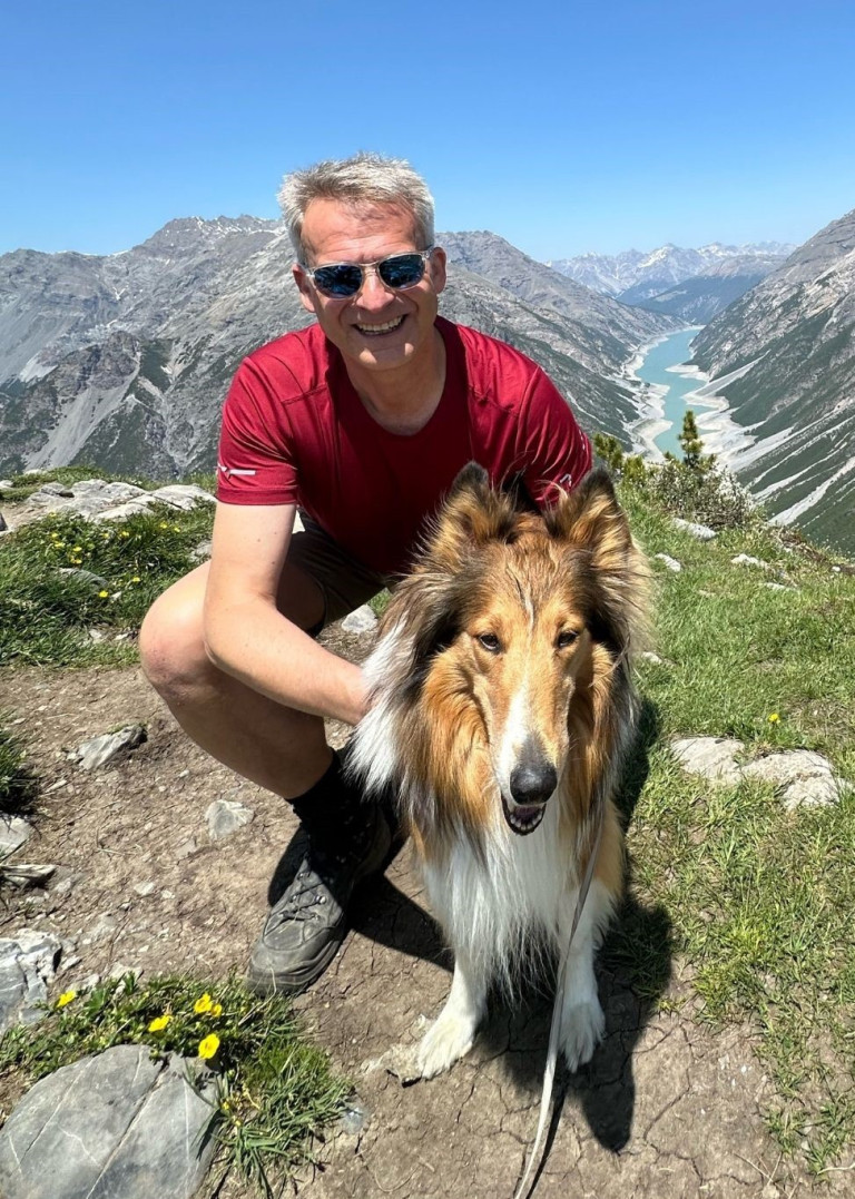 Wanderer mit Hund in den Bergen mit Blick auf einen See, ideales Lieblingsreiseziel für Naturliebhaber